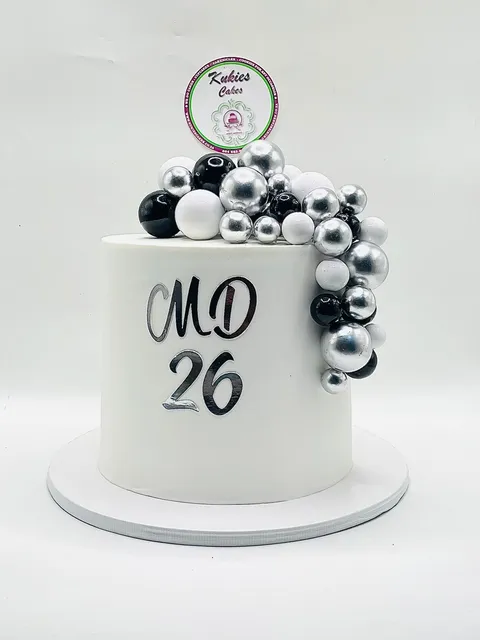 White cake with a cascading black, white and silver sphere garland and a mirror-silver birthday topper