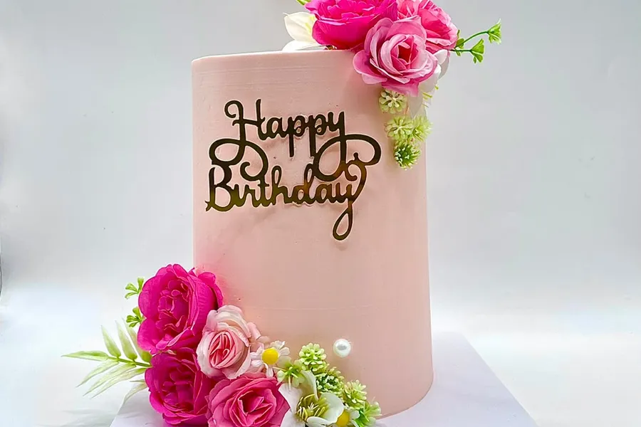 Blush pink cake with pink and white silk flower clusters and a gold script topper
