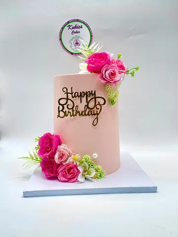 Blush pink cake with pink and white silk flower clusters and a gold script topper