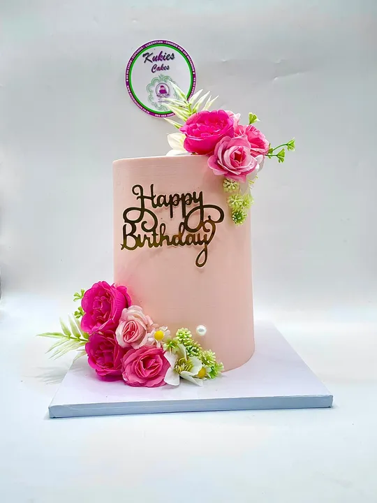 Blush pink cake with pink and white silk flower clusters and a gold script topper