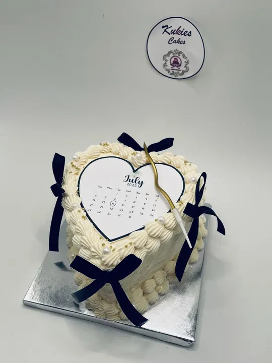 Cream heart shaped cake with a printed calendar topper and black ribbon bows