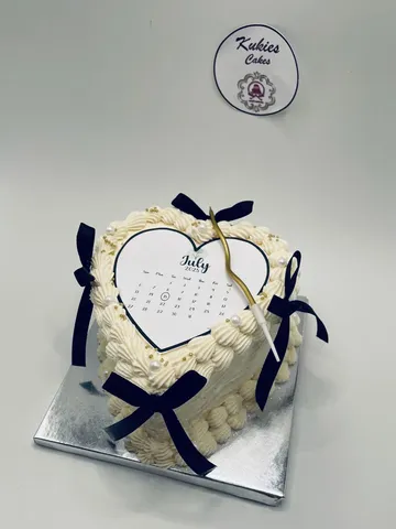 Cream heart shaped cake with a printed calendar topper and black ribbon bows