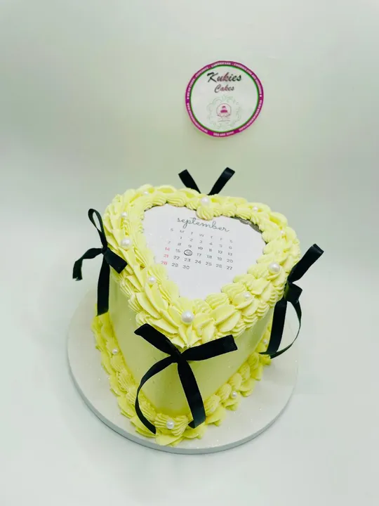Pale yellow heart shaped cake with a calendar topper and black ribbon bows
