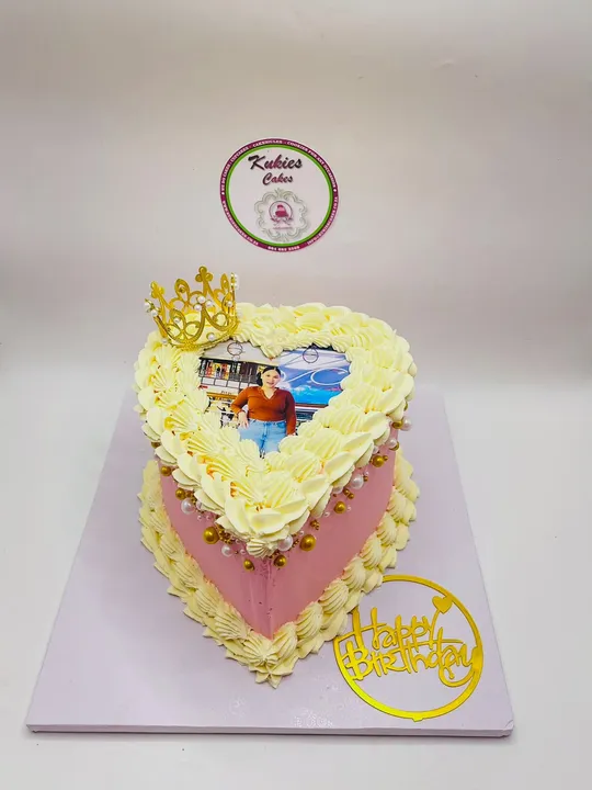 Pink and cream heart-shaped cake with a gold crown and Happy Birthday script topper