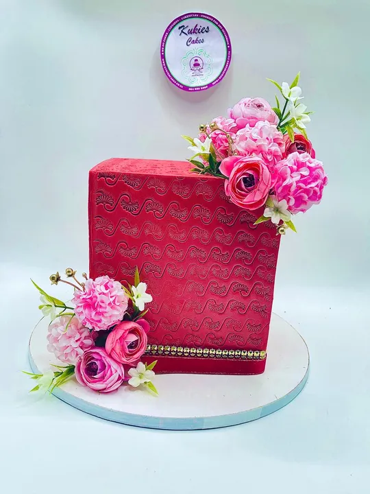 Red textured square cake with pink and white silk flowers and gold trim