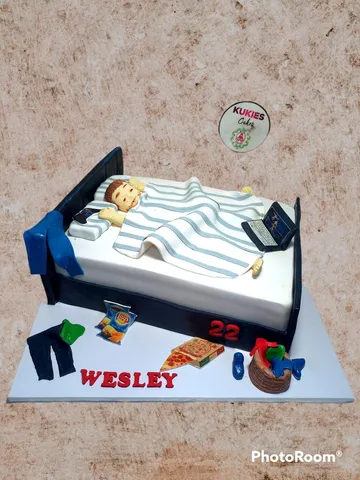 Novelty cake sculpted as a person sleeping in bed with snacks and a laptop