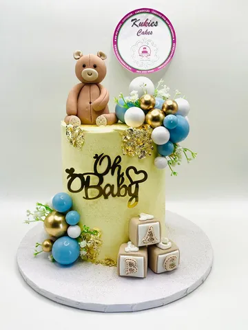 Pale yellow baby shower cake with a fondant teddy bear and alphabet blocks